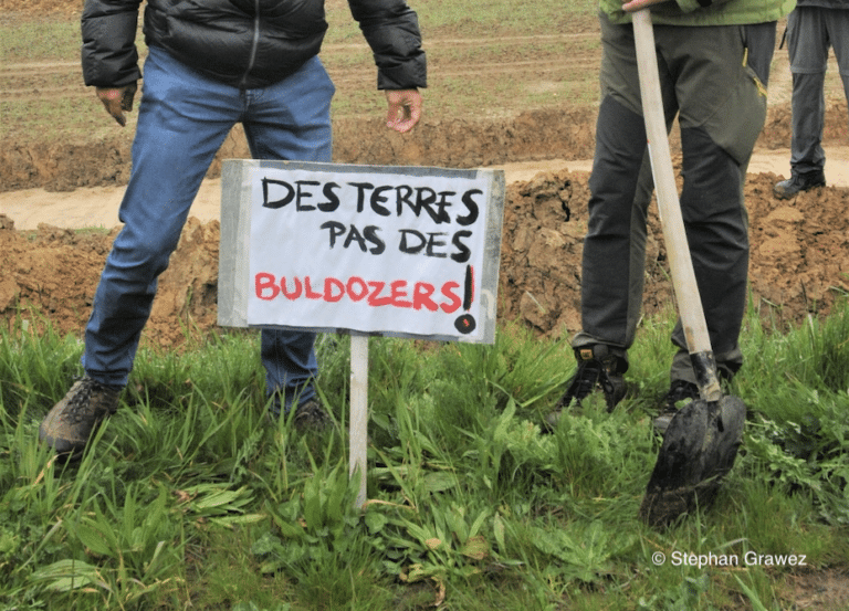 Une pancarte sur laquelle est écrit "des terres, pas des bulldozers"