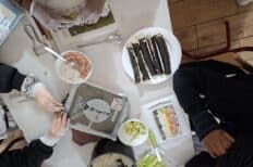 Une table avec de la nourriture posée dessus et des personnes qui cuisinent