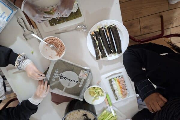 Une table avec de la nourriture posée dessus et des personnes qui cuisinent