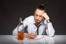 Un homme accoudé sur une table avec une bouteille devant lui
