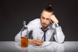 Un homme accoudé sur une table avec une bouteille devant lui