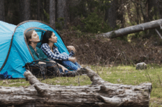 Deux jeunes filles assises à l'entrée d'une tente dans une forêt