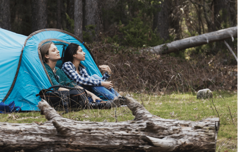 Deux jeunes filles assises à l'entrée d'une tente dans une forêt